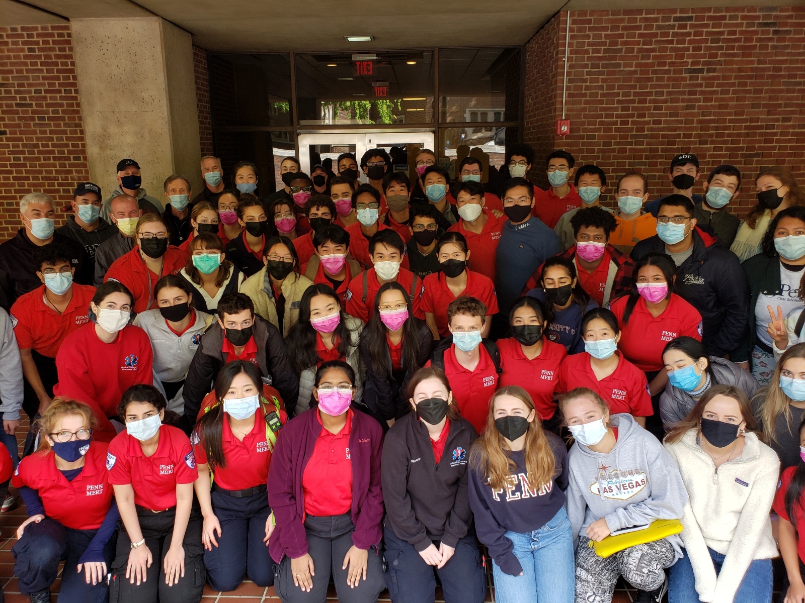 Group photo of over 60 MERT members, most are in their red polo shirt uniforms, posing with University administrators. Everyone is wearing a medical face mask.