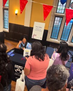 A police officer sits behind a table with resource materials, looking up at a student.