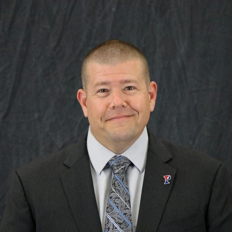 Photo of George Fox, with short, closely-shorn dark hair, wearing a black suit jacket, gray shirt and paisley patterned tie with blue stripes.