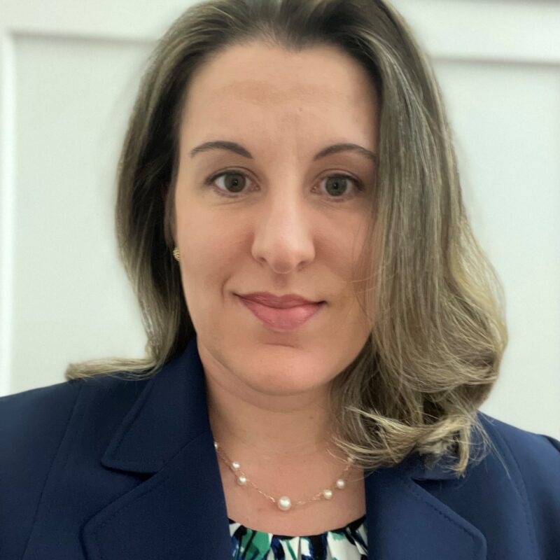 Photo of Nora Greenberg wearing a blue suit jacket and patterned blouse.