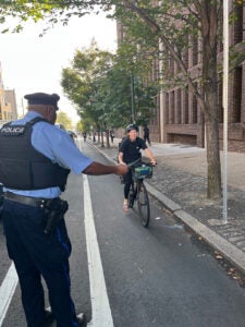An officer holds out a pamphlet to an approaching bicyclist who is smiling