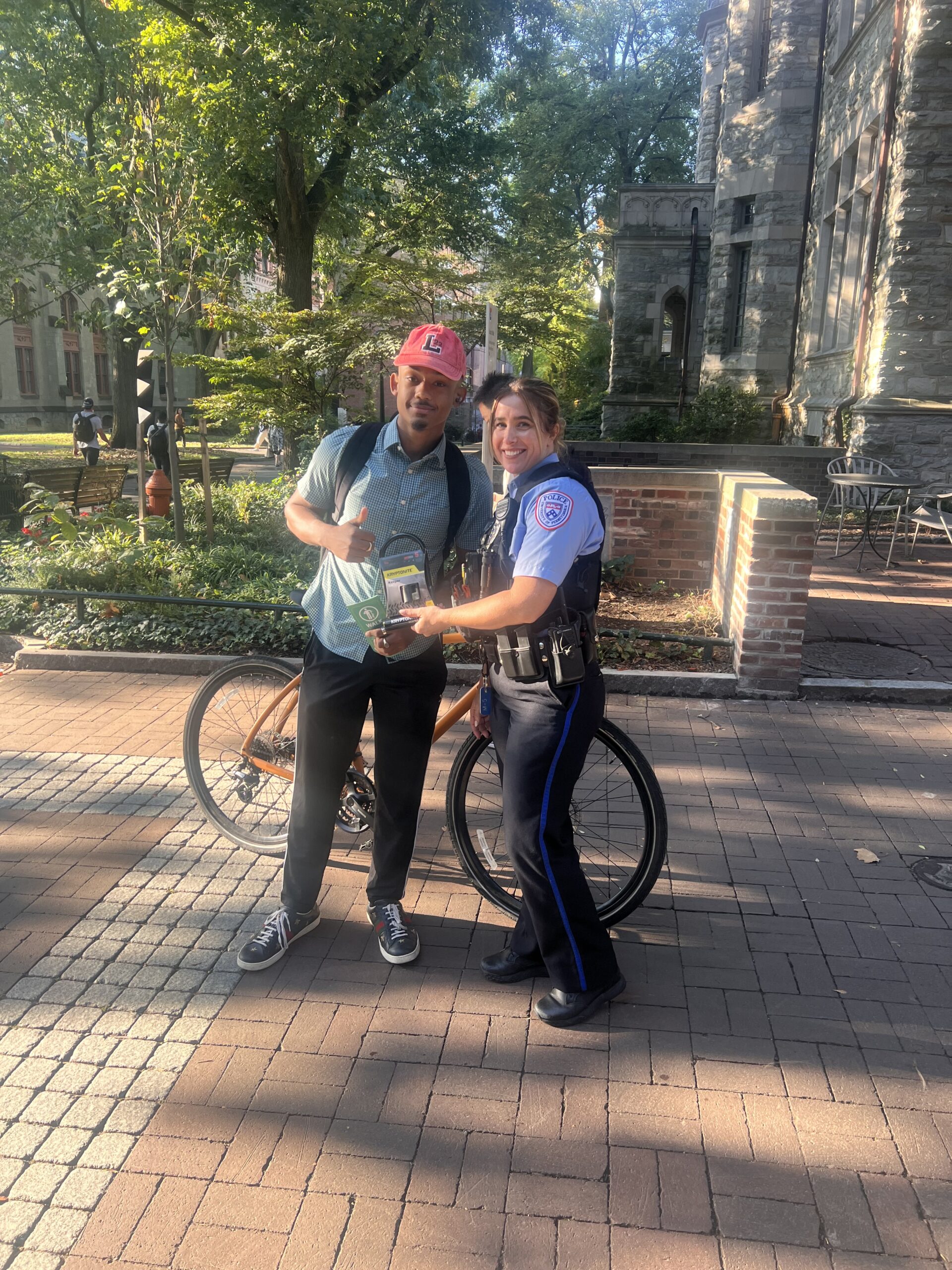 A bike rider poses with a police officer with a U-lock style bike lock and a share the road pamphlet.