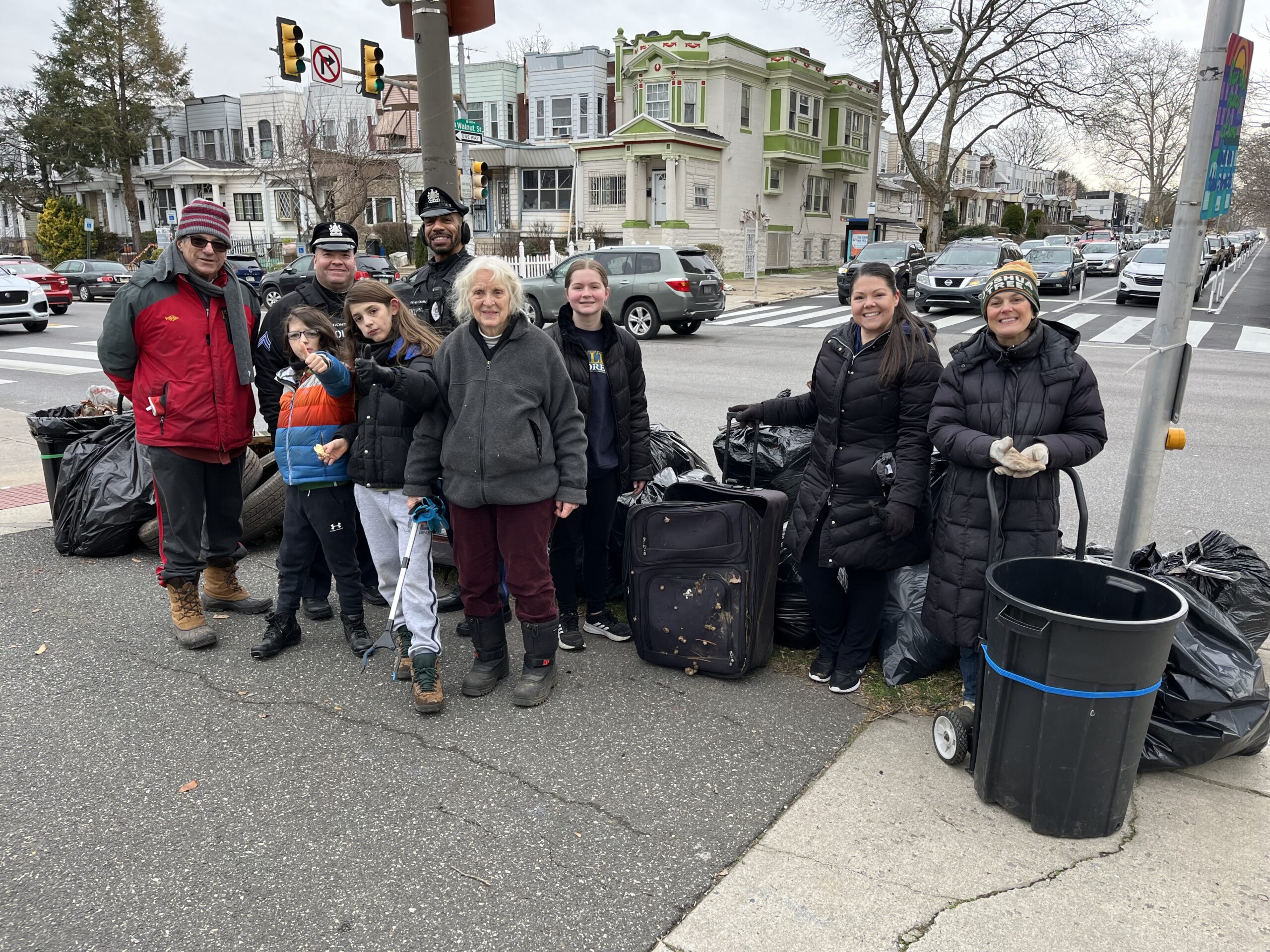 Two officers at a neighborhood clean up event, on Walnut Street with a group of volunteers, standing with the bags of garbage they collected.
