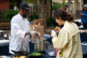 A PennDining chef serves a community member a cup of chili.