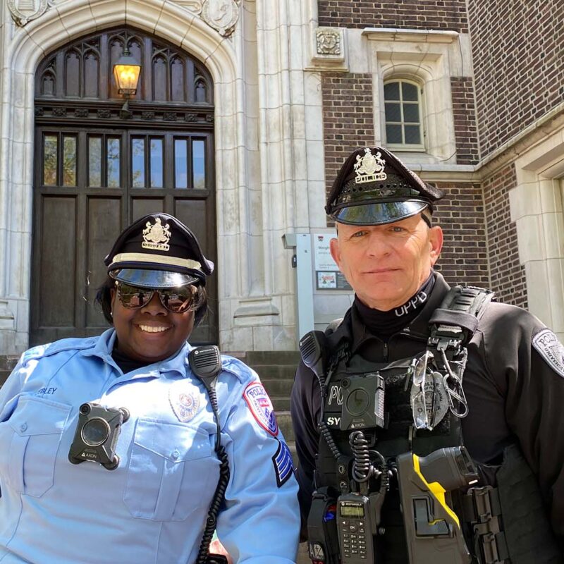 UPPD Officers in uniform smiling in front of brick building.