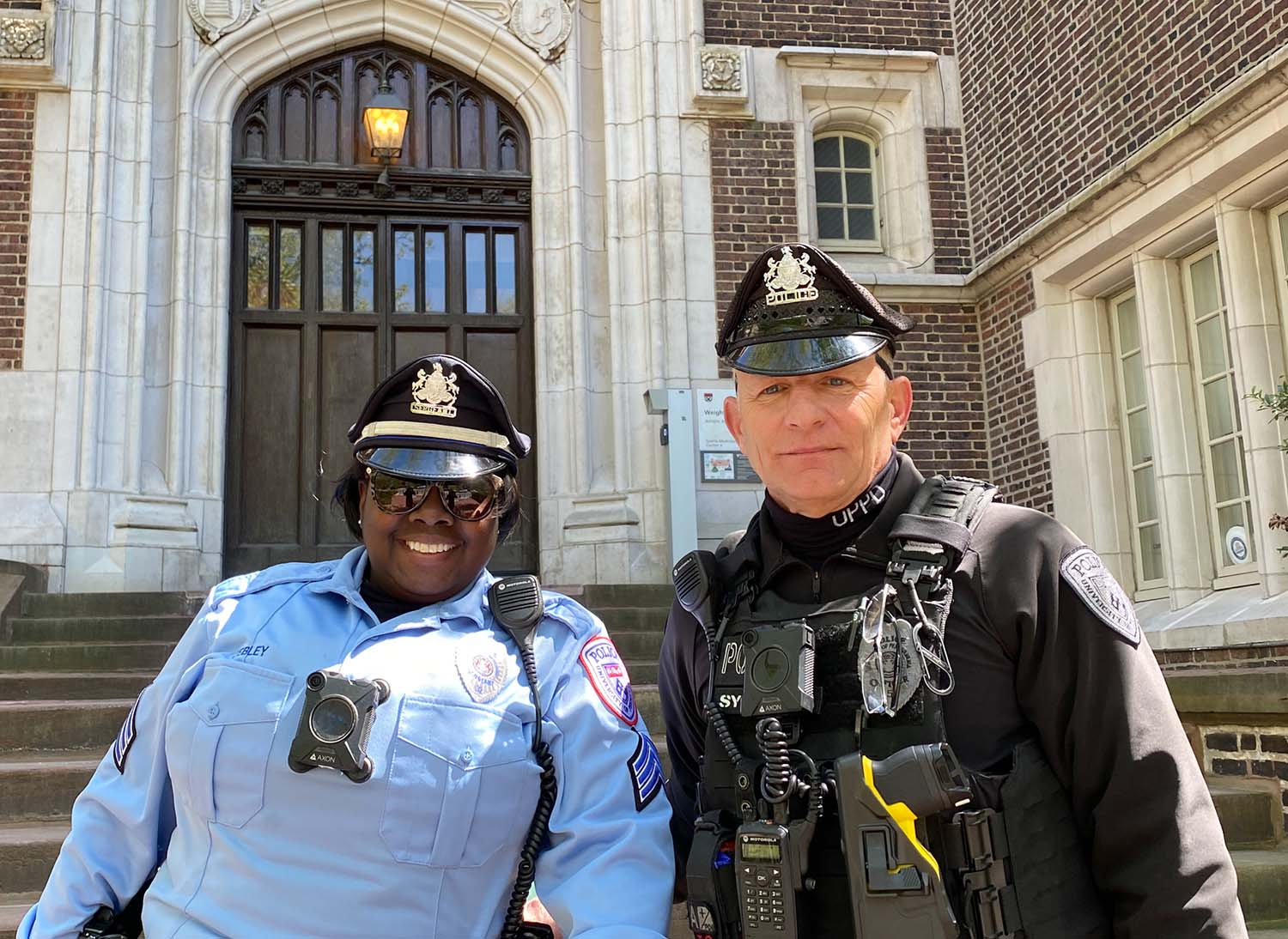 UPPD Officers in uniform smiling in front of brick building.