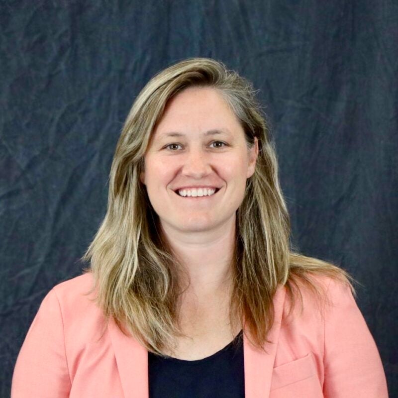 Photo of Paige Wigginton, she has blond hair, slightly longer than shoulder-length, wearing a pink suit jacket and black shirt.
