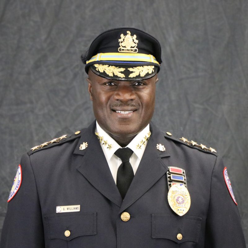 Photo of Gary Williams, wearing a police formal blousecoat, police hat with Chief emblem, white shirt with 4 gold stars on each side.